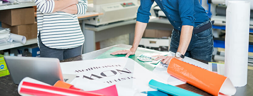 Two people at a desk looking at color samples and bright colored vinyl samples.