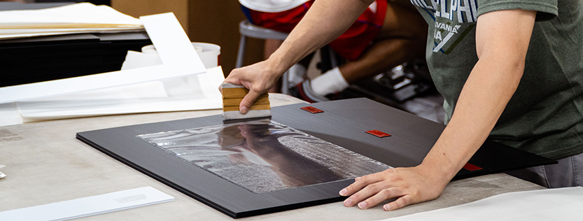 Print production finisher mounting a clear sheet onto a board.