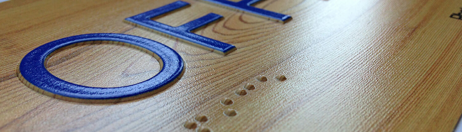 Close up of ADA signage (with braille) on a wood surface.