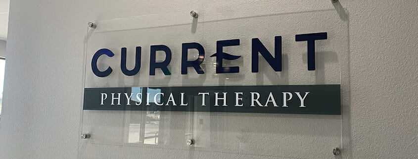 clear acrylic printed sign for Current Physical Therapy on wall with standoffs