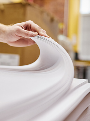 A person's hand flipping through a large stack of papers.