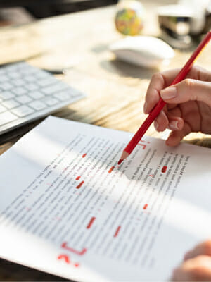 A person with a red pencil proofreading a document.