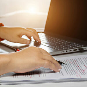 A person with a pen and pad plus a laptop computer.