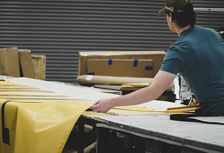 Man straightening and sewing a large vinyl banner.