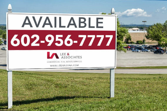 Property sign posted in green grass displaying information for commercial real estate company.