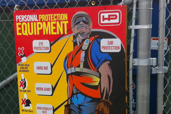 Construction sign attached to a chain link fence displaying PPE information.